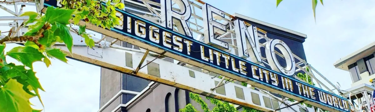 Blue metal sign reading 'Biggest Little City in the World' on building with green vines