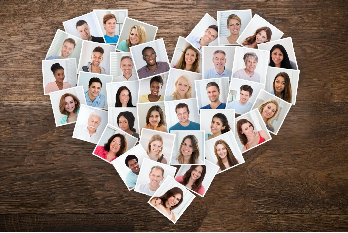 Multiple portrait photographs arranged in a heart shape on wooden surface